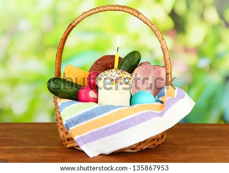 Easter basket: Conceptual photo of traditional easter food in wicker basket, on wooden table on bright background