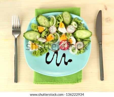 Fresh mixed salad with eggs, salad leaves and other vegetables on color plate, on wooden background