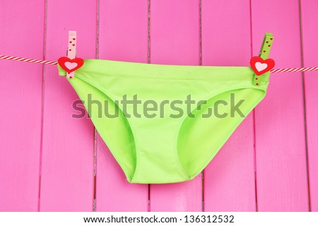 Womans panties hanging on a clothesline, on pink wooden background