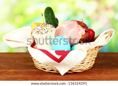 Easter basket: Conceptual photo of traditional easter food in wicker basket, on wooden table on bright background