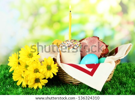 Easter basket: Conceptual photo of traditional easter food in wicker basket, on green grass, on bright background