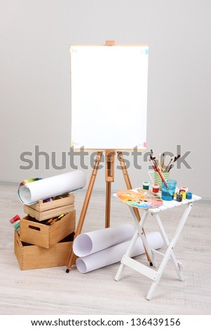 Wooden easel with clean paper and art supplies in room
