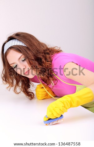 Young housewife cleaning up table at home on grey background