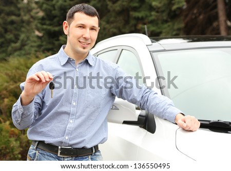 Portrait of happy man with car key, standing near the car