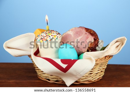Easter basket: Conceptual photo of traditional easter food in wicker basket, on wooden table on color background