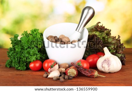 Composition of mortar,spices, tomatoes and  green herbs, on bright background