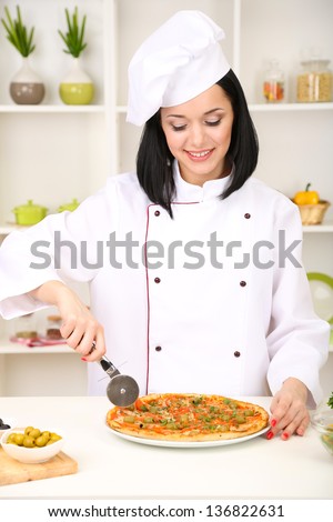 Beautiful girl chief-cooker with pizza on kitchen background