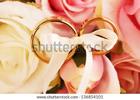 Wedding rings tied with ribbon on rose background