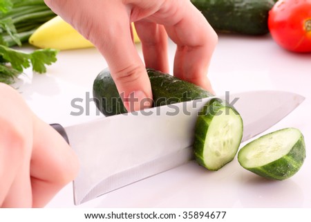 Someone cutting a cucumber, and slice flying isolated on white