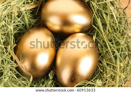Three golden hen\'s eggs in the grassy nest on the wooden table