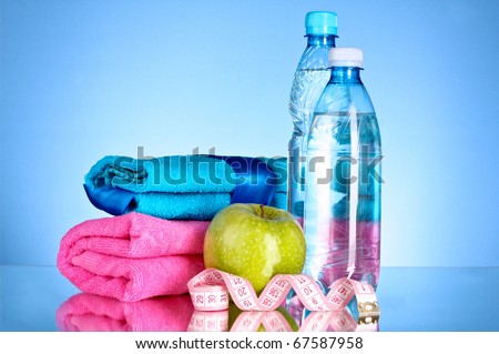 Blue bottle of water, apple, sports towel and measure tape on blue background