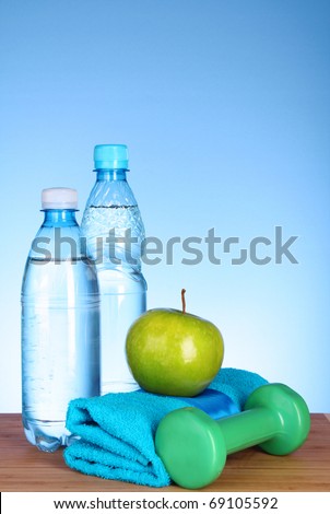 Blue bottle of water, apple, sports towel,dumbbells and measure tape on blue background