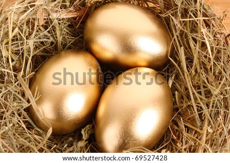 Three golden hen's eggs in the grassy nest on the wooden table