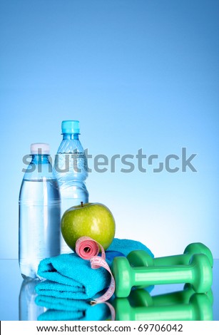 Blue bottle of water, apple, sports towel,dumbbells and measure tape on blue background