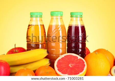 bottles of juice  with ripe fruits on yellow background