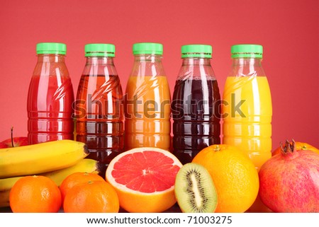bottles of juice  with ripe fruits on red background