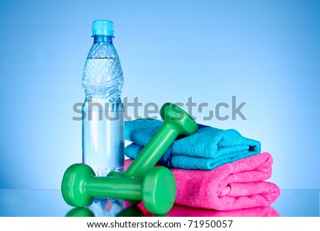 Blue bottle of water, sports towel, measure tape and dumbbells on blue background