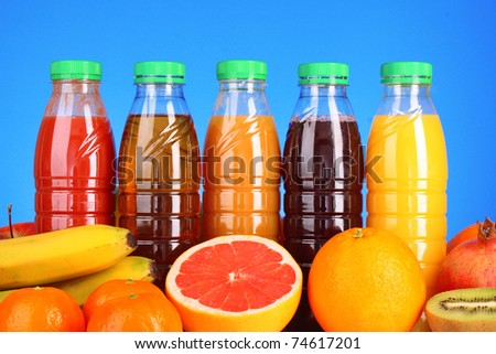 bottles of juice  with ripe fruits on blue background