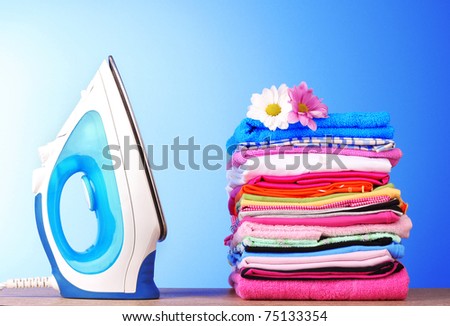 Pile of colorful clothes and electric iron  on blue background