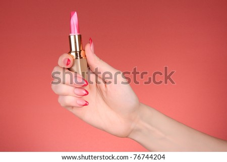 Red lipstick in hand on red background
