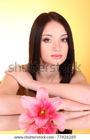 Beautiful young woman with lily flower on yellow background with mirror