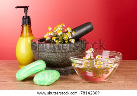 Mortar and pestle with soap and flowers on red background
