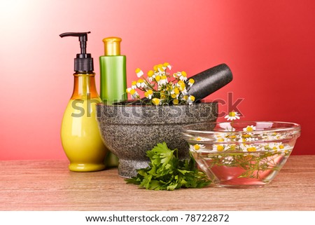 Mortar and pestle with soap and flowers on red background