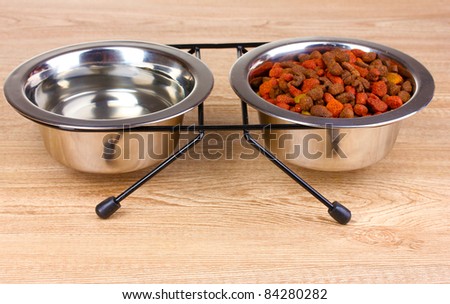 Dry cat food and water in bowls on wooden background