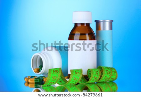 Diet pills and measuring tape on blue background
