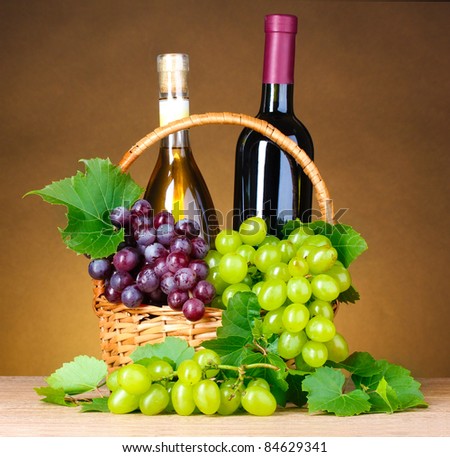 Bottles of wine and grapes in basket on yellow background
