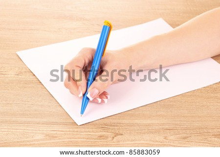 Women's hand, a pen and paper on wooden background