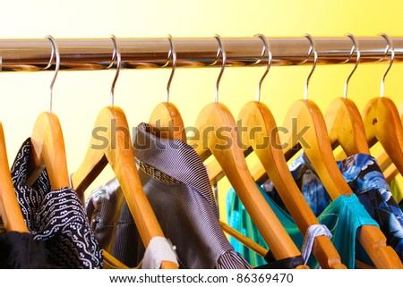 different clothes on wooden hangers on yellow background