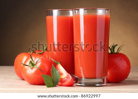 Tomato juice in glasses and tomato on wooden table on brown background