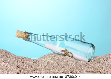 Glass bottle with note inside on sand on blue background