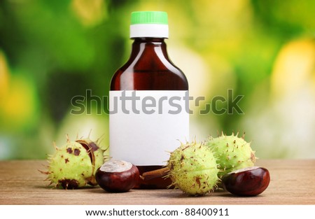 chestnuts and medical bottle on wooden table on green background