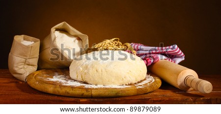 Dough and bags with flour on wooden table on brown background