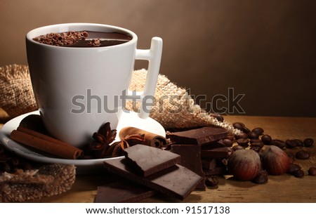 cup of hot chocolate, cinnamon sticks, nuts and chocolate on wooden table on brown background