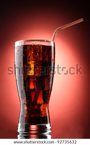Glass of cola with ice on red background