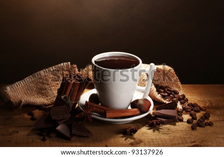cup of hot chocolate, cinnamon sticks, nuts and chocolate on wooden table on brown background