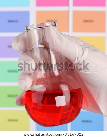 Flask with red liquid in hand on color samples background