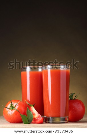 Tomato juice in glass and tomato on wooden table on brown background