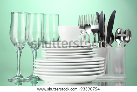 Clean plates, glasses, cup and cutlery on green background