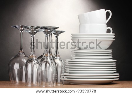 Clean plates, glasses and cups on wooden table on grey background