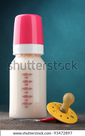 bottle of milk and soother on wooden table on blue background