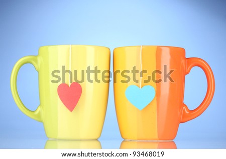 Two cups and tea bags with red and blue heart-shaped label on blue background