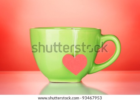 Green cup and tea bag with red heart-shaped label on red background