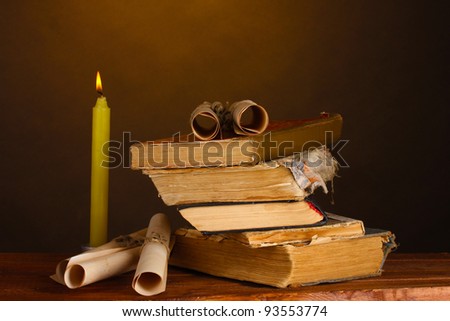 Pile of old books with candle and scroll on brown
