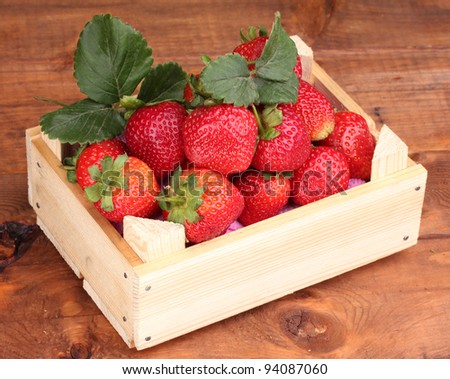 Strawberries with leaves in wooden box on wooden  background