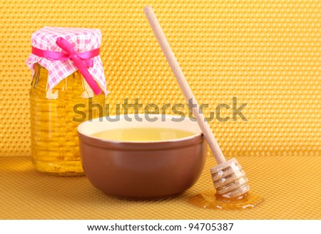 Jar of honey, bowl and wooden drizzler with honey on yellow honeycomb background