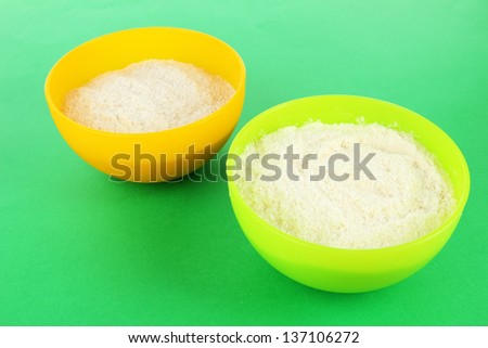 Powdered milk in bowls for baby on green background